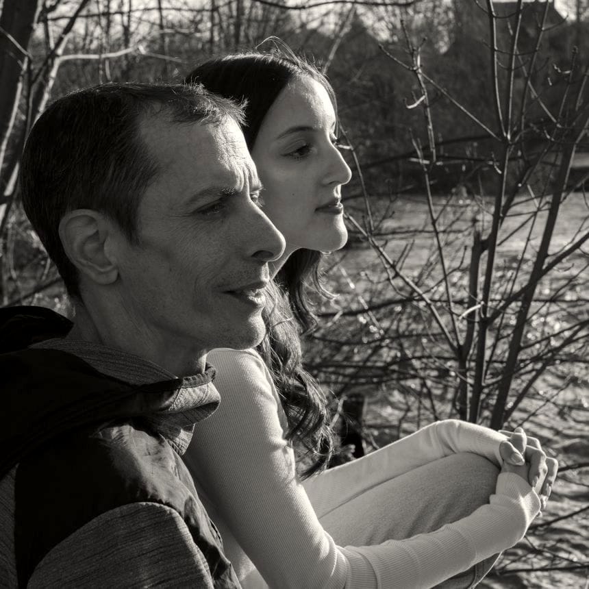 Andy Perkins, age 48, sits next to his teenage daughter Addison, both of their heads turned to show the profiles of their faces. They are sitting next to some leafless trees and a body of water.