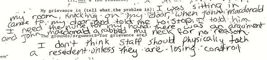 An excerpt from the ombudsman form Andy Perkins filled out by hand after the June 1993 incident. In type, the form reads: “My grievance is (tell what the problem is):” Andy writes: “I was sitting in my room, knocking on my door, when John Macdonald came to my door and told me to stop. I told him I need the nurse for my hand. There was an argument and John Macdonald grabbed my neck for no reason.” The next line on the form reads: “The grounds/arguments for grievance are:” Andy writes: “I don’t think staff should physically touch a resident unless they are losing control.”